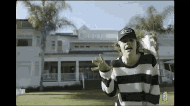 a man in a black and white striped sweater is standing in front of a house
