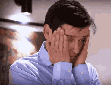 a man in a blue shirt is holding his head with his hands