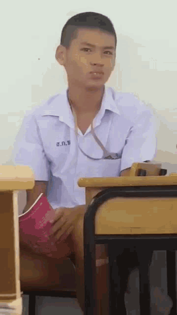 a boy in a school uniform is sitting at a desk with a book in his hand .
