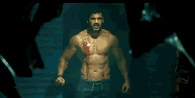 a shirtless man is standing in a dark room next to a table .