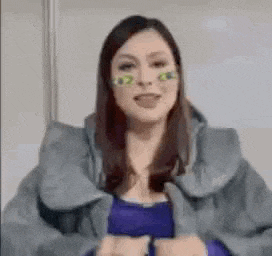 a woman wearing a gray jacket and a purple shirt is holding her breasts .