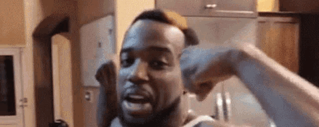 a man is flexing his muscles in a kitchen and making a funny face .