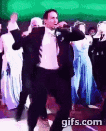 a man in a suit is singing into a microphone while dancing in front of a crowd .
