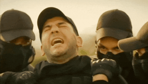 a man is being held by a group of men wearing black hats and masks
