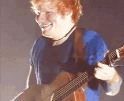 a man in a blue shirt is smiling while playing an acoustic guitar