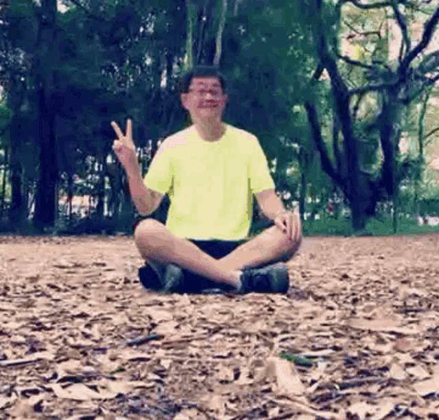 a man in a yellow shirt is sitting on a pile of leaves and giving a peace sign .