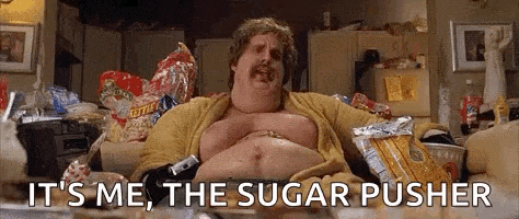 a fat man is sitting on a couch in a messy room eating chips and candy .