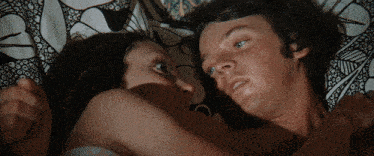 a man and a woman laying on a bed with a patterned blanket