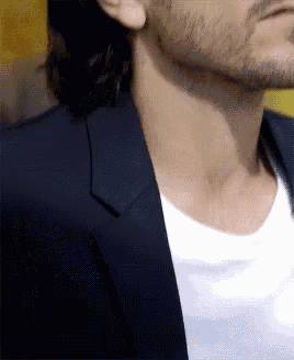 a man with long hair and a beard is wearing a black suit jacket and a white t-shirt