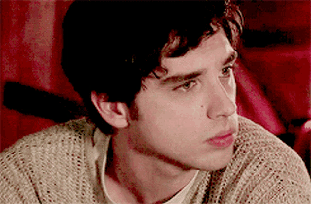 a close up of a young man 's face wearing a tan sweater