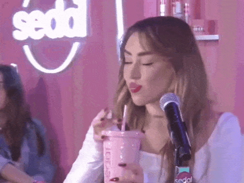 a woman is sitting in front of a microphone drinking from a pink cup .