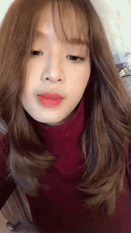 a woman wearing a red turtleneck and red lipstick is taking a selfie