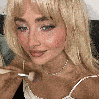 a woman is applying makeup with a brush on her face