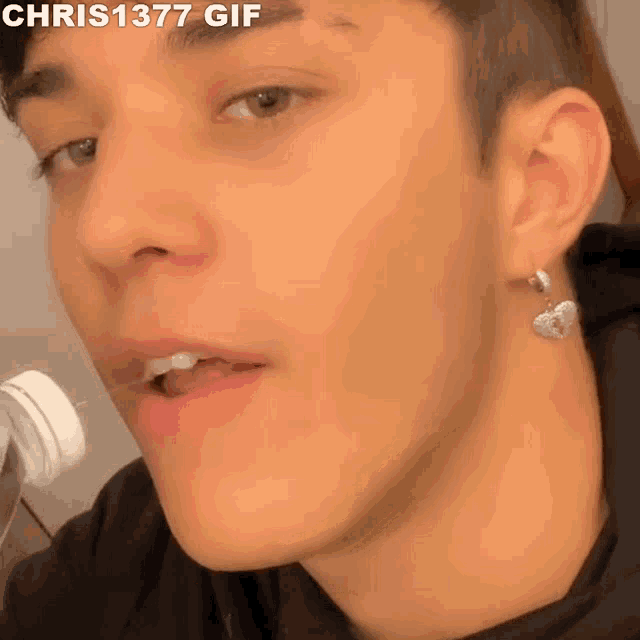 a close up of a man 's face with a bottle in his mouth and a heart shaped earring .