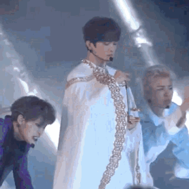 a man in a white cape is singing into a microphone on a stage with other people .