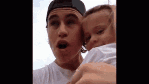 a young man is holding a baby in his arms and making a funny face .