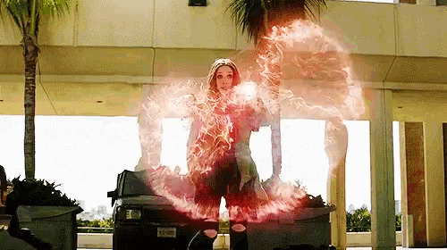 scarlet witch is standing in front of a building with a car in the background and using a spell .