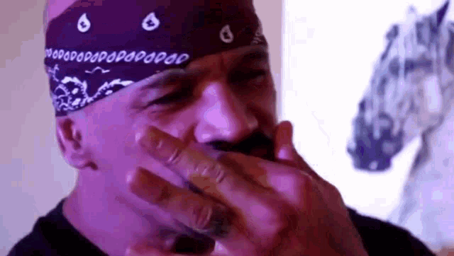 a man wearing a purple bandana is smoking a cigarette in front of a horse statue .