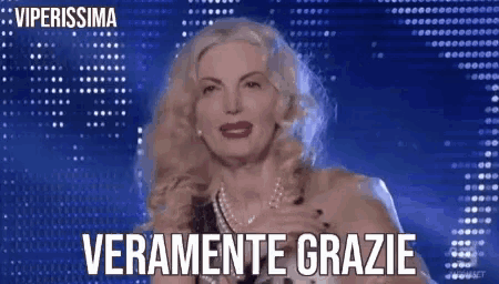 a woman with blonde hair is standing in front of a blue background and says ' veramente grazie ' .