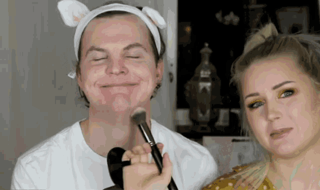 a woman applying makeup to a man 's face with a brush
