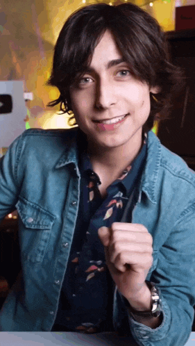 a young man wearing a denim shirt and a tie is smiling