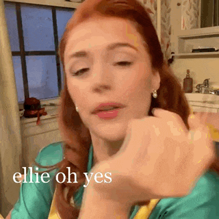 a woman with red hair is applying makeup to her face in a kitchen .
