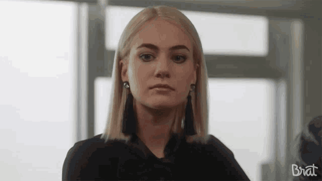 a woman with blonde hair is wearing earrings and a black shirt with the word brat on the bottom