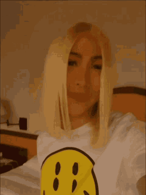 a woman is wearing a white t-shirt with a yellow smiley face on it .