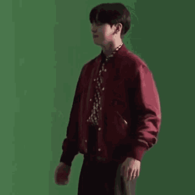 a young man wearing a red jacket and a black shirt is standing in front of a green screen .