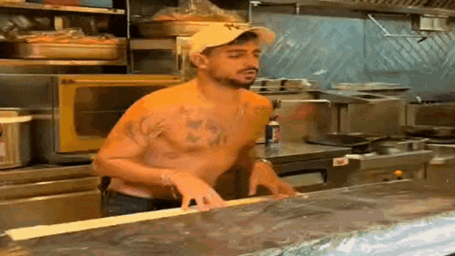 a man without a shirt is standing in a kitchen .