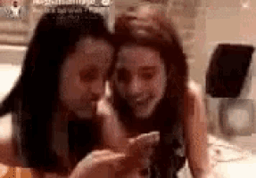 two women are laying next to each other on a bed .