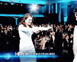 a woman in a white dress is dancing in front of a crowd at a hollywood awards