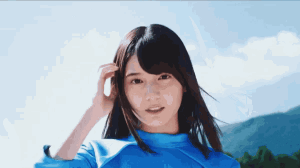 a young woman in a blue shirt holds her hand to her head