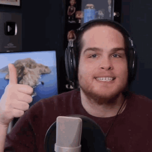 a man wearing headphones gives a thumbs up in front of a microphone