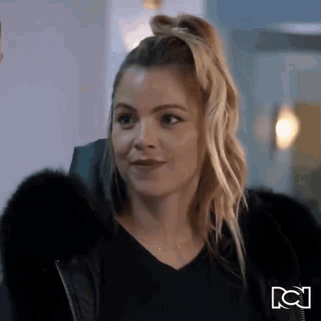 a woman with blonde hair is wearing a black fur coat and a black sweater .