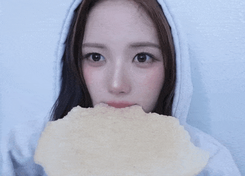 a woman in a white hoodie is holding a piece of food in front of her face