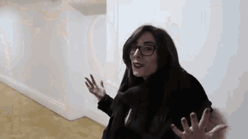 a woman with glasses is standing in a hallway with her arms outstretched