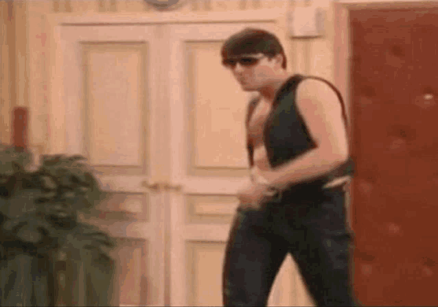 a man wearing sunglasses and a vest is standing in a room .