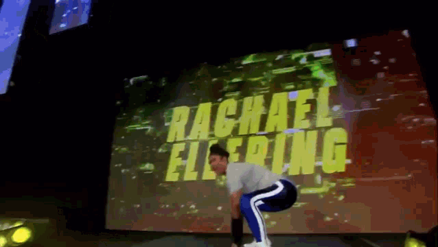 a man is squatting down in front of a large screen that says rachael elering