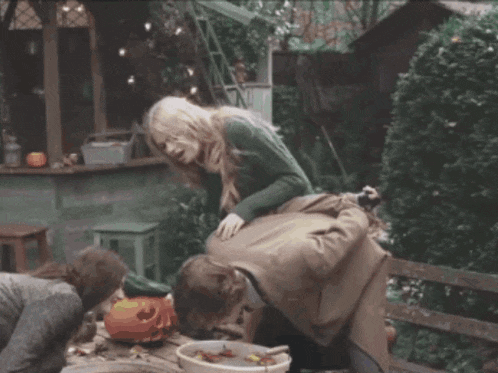 a woman in a green sweater sits on a man 's back in a garden