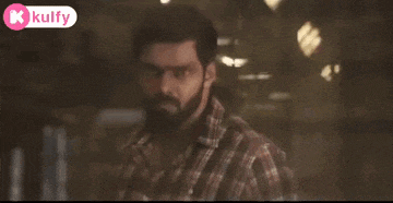 a man with a beard and a plaid shirt is standing in a dark room .
