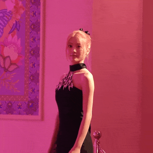 a woman in a black dress is standing in front of a pink wall with korean writing on it