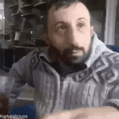 a man with a beard wearing a grey sweater is looking at the camera