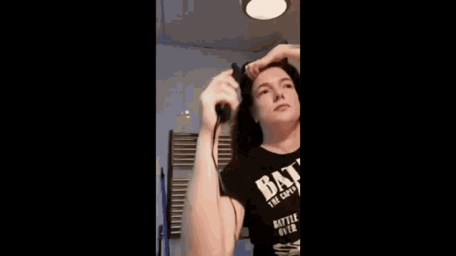 a woman wearing a batman t-shirt is holding her hair in her hand .