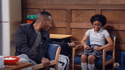 a man and a girl are sitting in chairs in a waiting room .