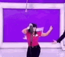a woman is singing into a microphone while dancing in front of a purple wall .