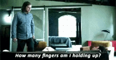 a man standing in a living room asking how many fingers am i holding up ..