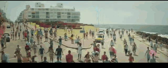 a large group of people are walking down a street in front of the ocean