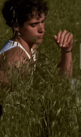 a young man is sitting in a field of tall grass and smelling the grass .