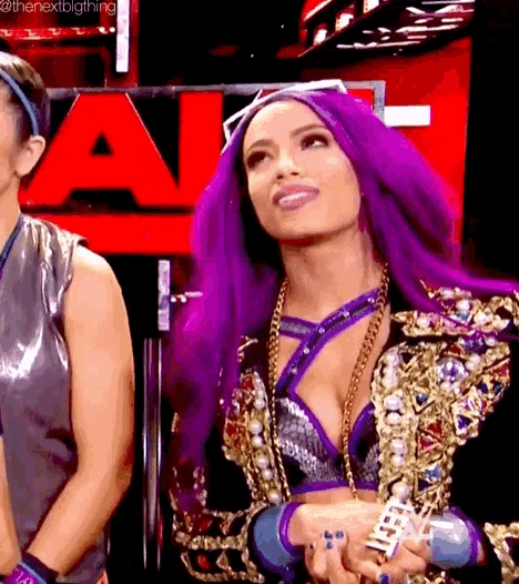 a woman with purple hair is standing next to another woman in front of a red sign .